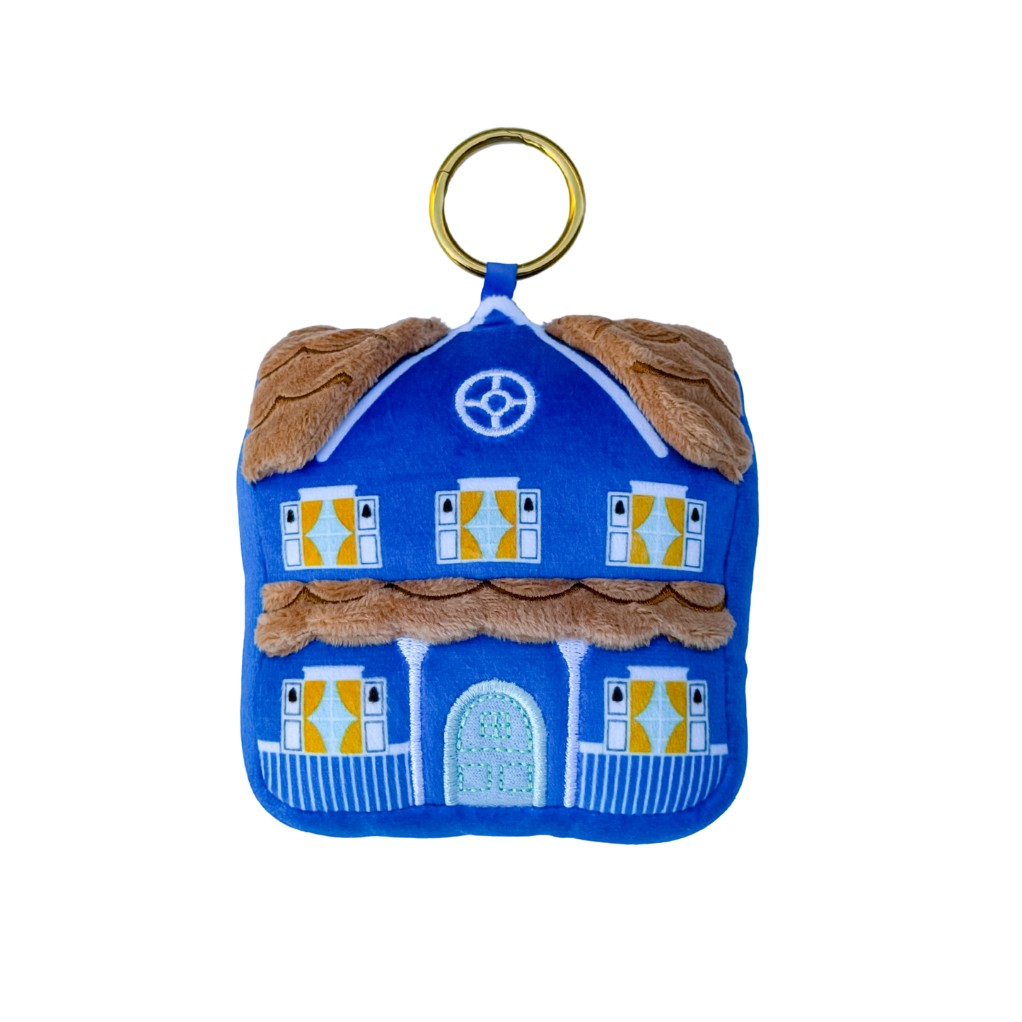 A blue felt house-shaped keychain or bag charm with a gold metal ring, featuring brown faux-fur trim, yellow window shutters, and a light blue front door on a white background.